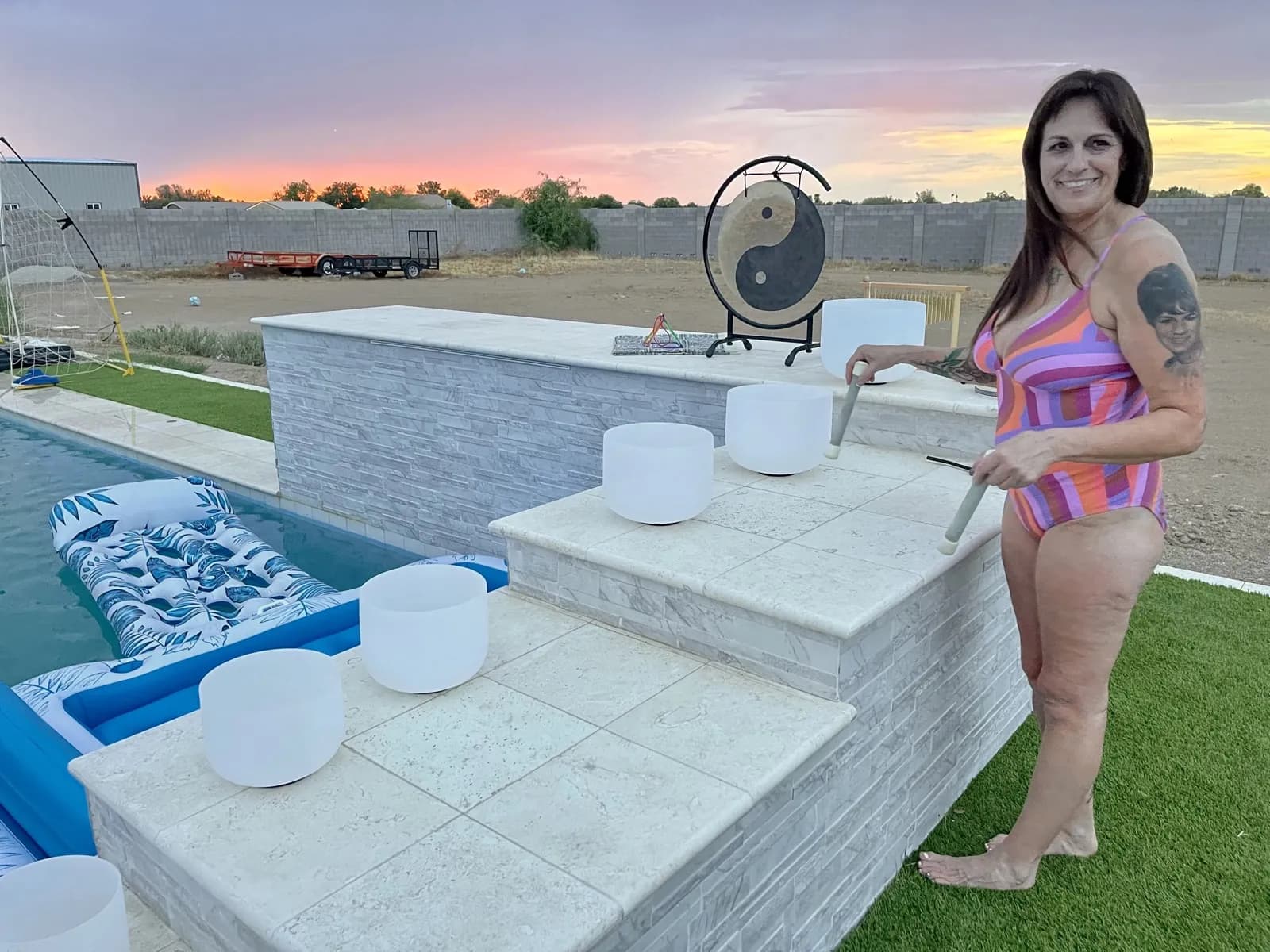 Victoria with singing bowls and gong by the pool at sunset